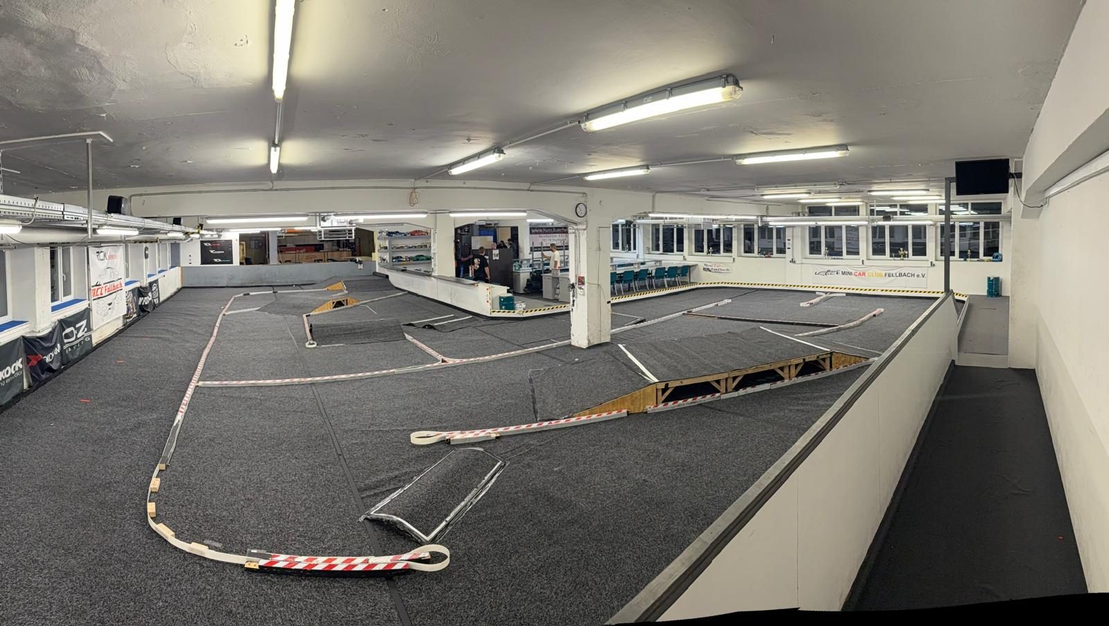 Die Halle des MCC Fellbach mit grauem Teppich, Rampen und rot-weißen Banden, hinten das Fahrerlager